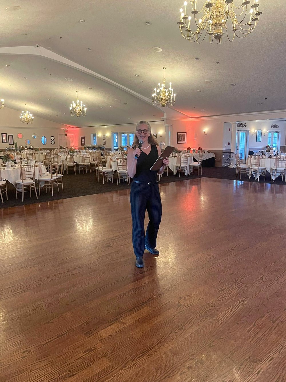 Jennifer Brown emceeing an event, microphone in hand, on the dance floor of a ballroom